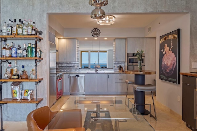 kitchen with tasteful backsplash, sink, gray cabinetry, light tile patterned floors, and stainless steel appliances