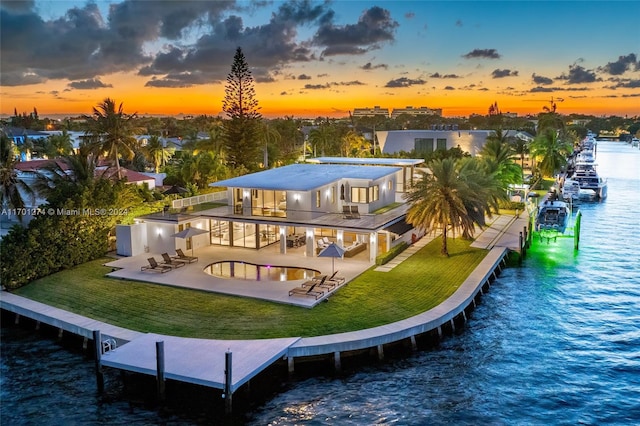 back house at dusk with a patio, a water view, a balcony, and a lawn