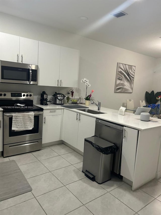 kitchen with kitchen peninsula, appliances with stainless steel finishes, sink, light tile patterned floors, and white cabinetry