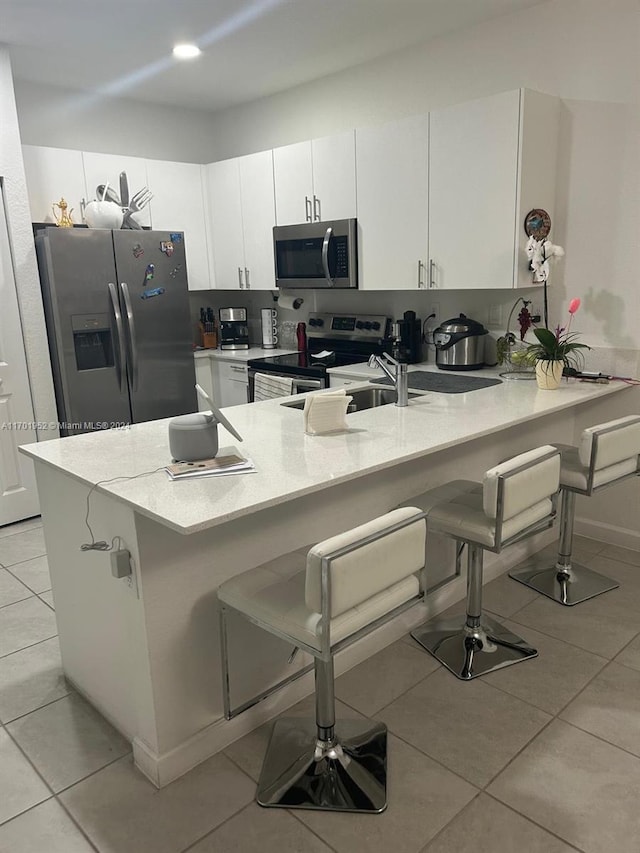 kitchen with stainless steel appliances, light tile patterned floors, kitchen peninsula, a kitchen bar, and white cabinets