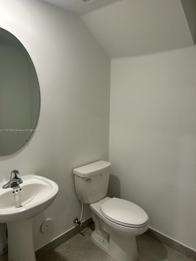 bathroom with tile patterned flooring, toilet, lofted ceiling, and sink