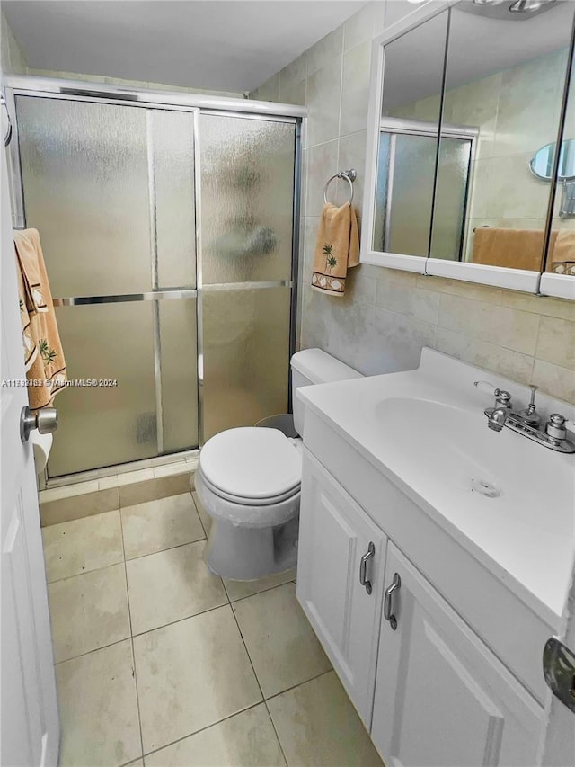 bathroom with tile patterned floors, an enclosed shower, vanity, tile walls, and toilet