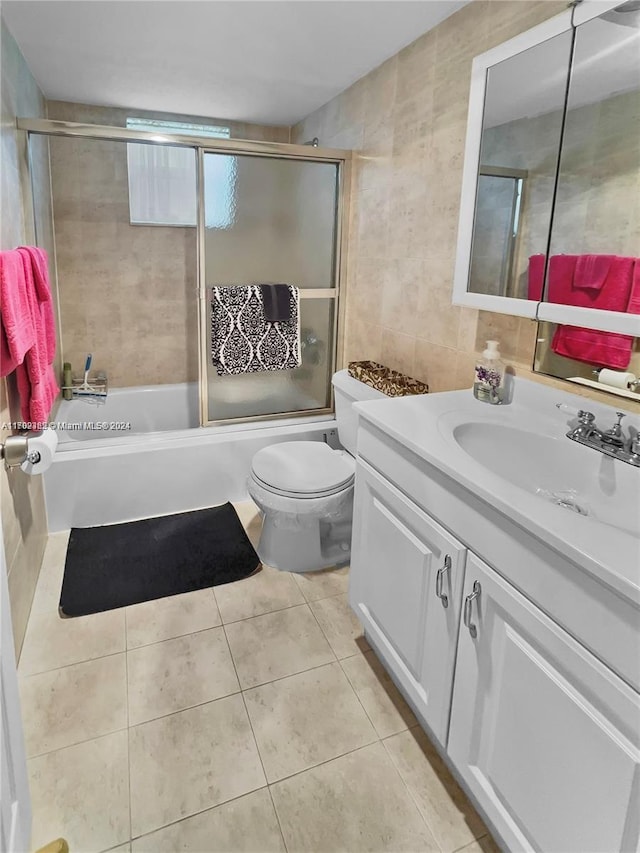 full bathroom with tile patterned flooring, combined bath / shower with glass door, toilet, vanity, and tile walls