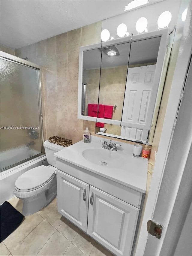 full bathroom with tile patterned flooring, combined bath / shower with glass door, toilet, vanity, and tile walls