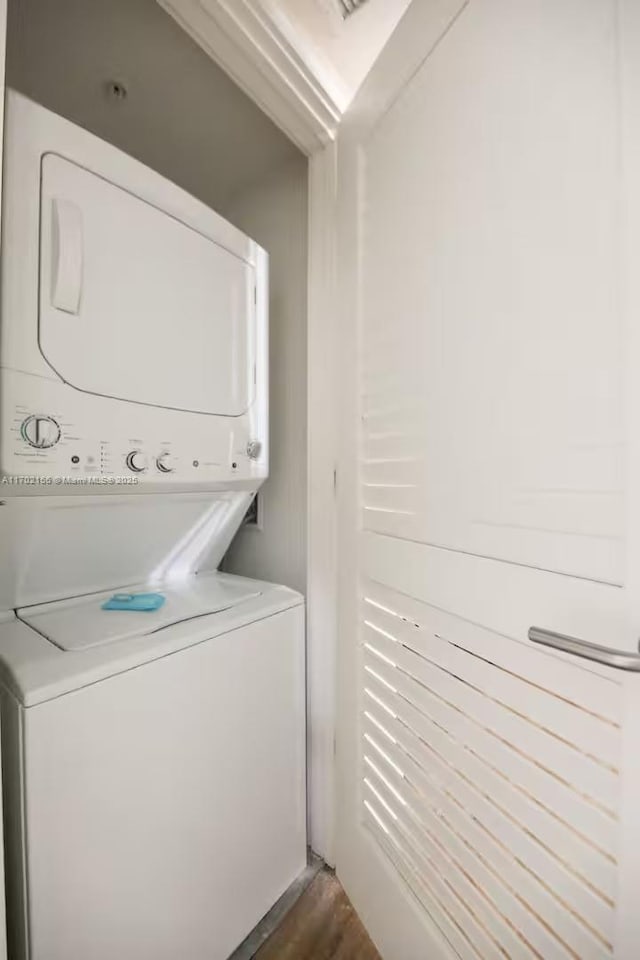 clothes washing area featuring laundry area, dark wood-style flooring, and stacked washer and clothes dryer