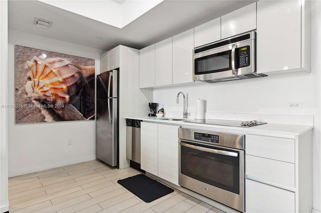 kitchen with white cabinets, appliances with stainless steel finishes, light wood-type flooring, and sink