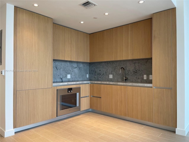 kitchen featuring oven, light wood-type flooring, and backsplash