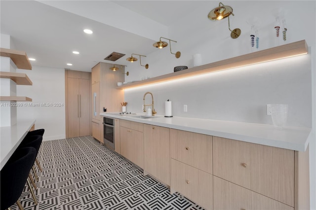 kitchen with black electric stovetop, stainless steel oven, sink, and light brown cabinetry