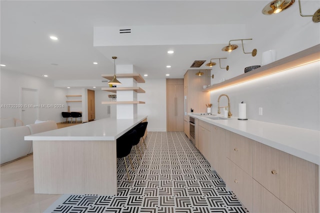 kitchen with light tile patterned flooring, light brown cabinetry, hanging light fixtures, and sink