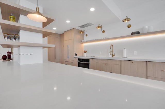 kitchen with light brown cabinets, oven, decorative light fixtures, and sink