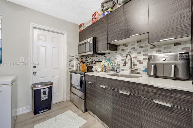 kitchen featuring sink, stainless steel appliances, backsplash, dark brown cabinets, and light wood-type flooring