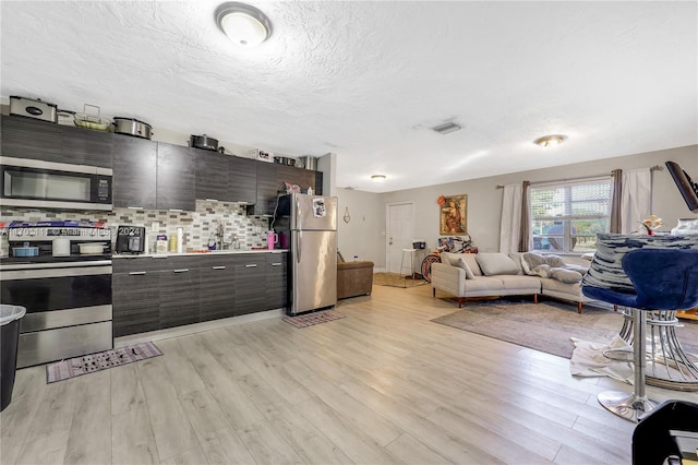 kitchen with decorative backsplash, a textured ceiling, dark brown cabinetry, stainless steel appliances, and light hardwood / wood-style flooring