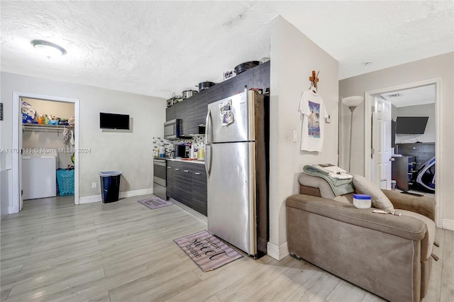 kitchen with a textured ceiling, stainless steel appliances, washer / clothes dryer, and light hardwood / wood-style floors