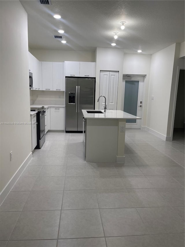 kitchen with white cabinetry, a textured ceiling, a center island with sink, light tile patterned flooring, and appliances with stainless steel finishes