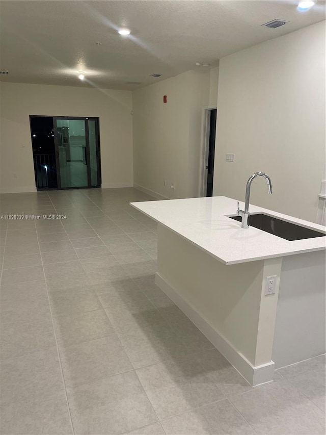 kitchen featuring light tile patterned floors, a center island with sink, and sink