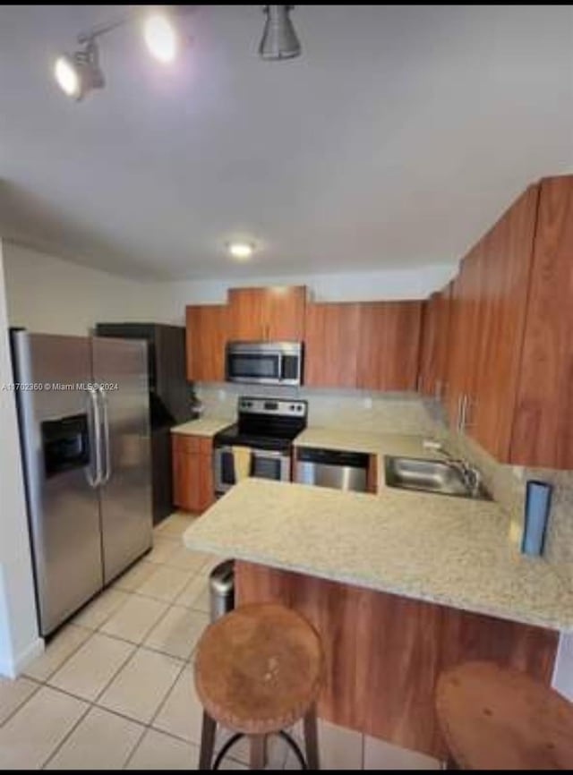 kitchen with a peninsula, a sink, light countertops, appliances with stainless steel finishes, and brown cabinetry