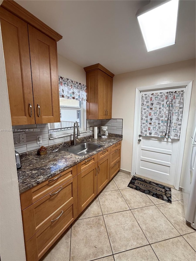 kitchen with backsplash, light tile patterned floors, sink, and dark stone counters