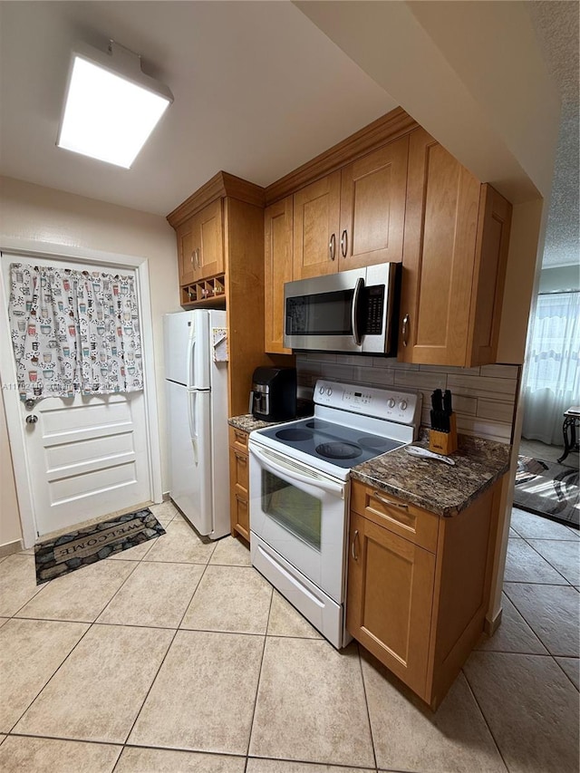 kitchen with white appliances, tasteful backsplash, dark stone countertops, and light tile patterned flooring