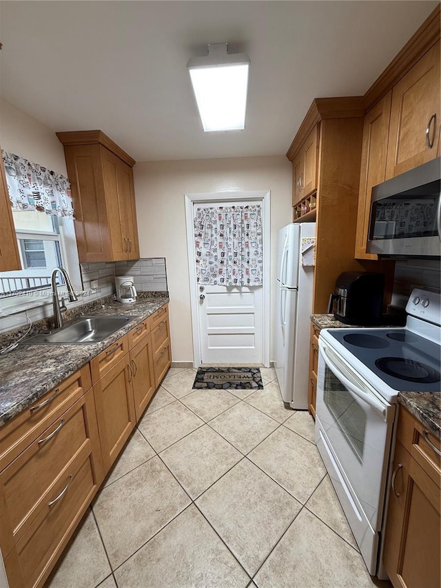 kitchen with light tile patterned flooring, dark stone countertops, white appliances, and sink