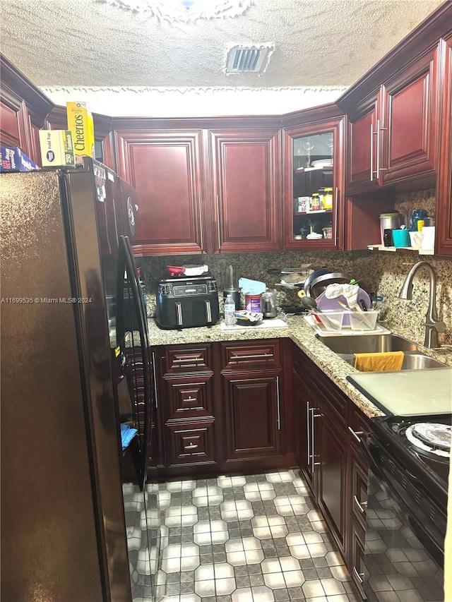 kitchen with backsplash, black appliances, sink, a textured ceiling, and light stone counters