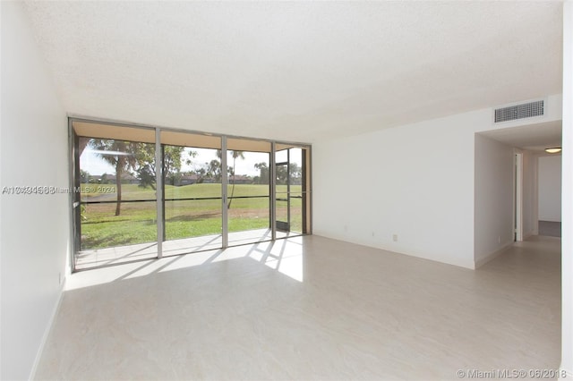 empty room with floor to ceiling windows, a rural view, and a textured ceiling