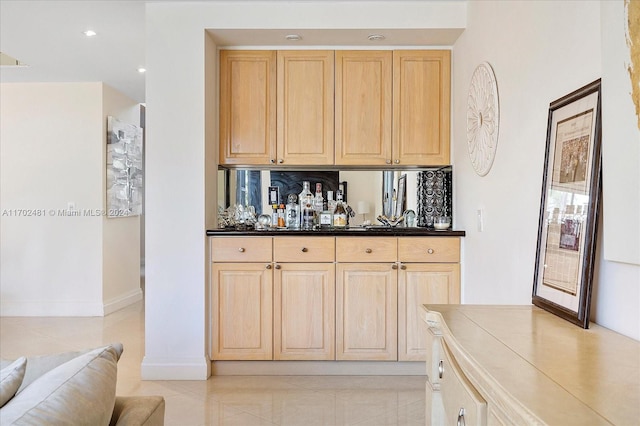 bar featuring light brown cabinets, light tile patterned floors, and sink