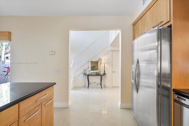 kitchen with stainless steel fridge with ice dispenser, light tile patterned floors, and dark stone counters