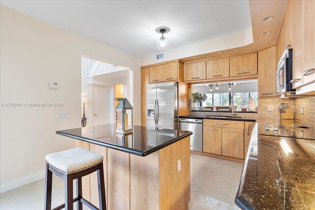 kitchen with sink, dark stone countertops, appliances with stainless steel finishes, tasteful backsplash, and a kitchen island