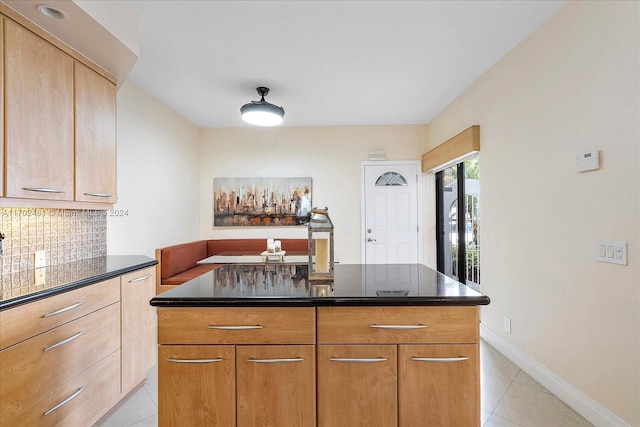 kitchen with a center island, dark stone countertops, light tile patterned floors, and backsplash