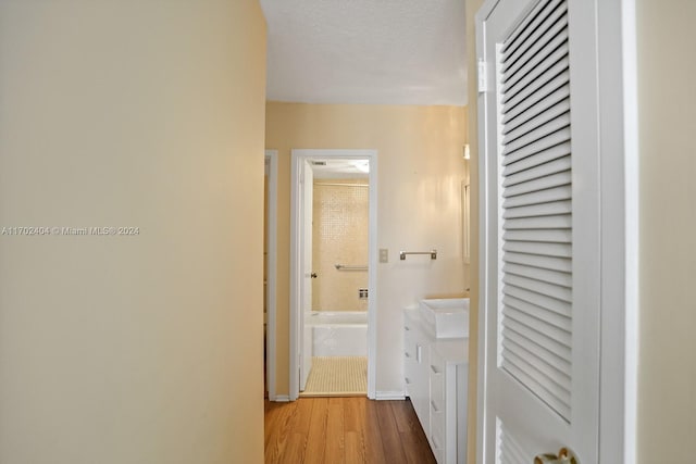 hall with sink, a textured ceiling, and light wood-type flooring