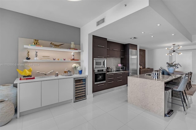 kitchen featuring white cabinetry, wine cooler, built in appliances, a breakfast bar, and dark brown cabinets