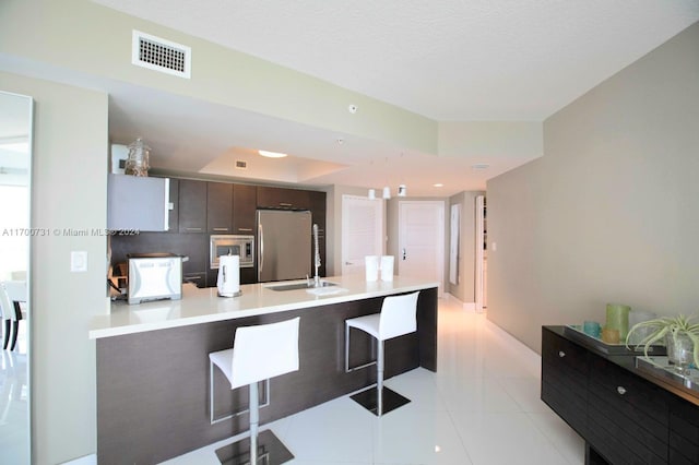 kitchen with a kitchen bar, kitchen peninsula, stainless steel appliances, sink, and light tile patterned flooring