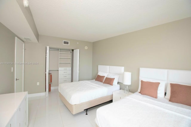 tiled bedroom featuring a walk in closet, a textured ceiling, and a closet