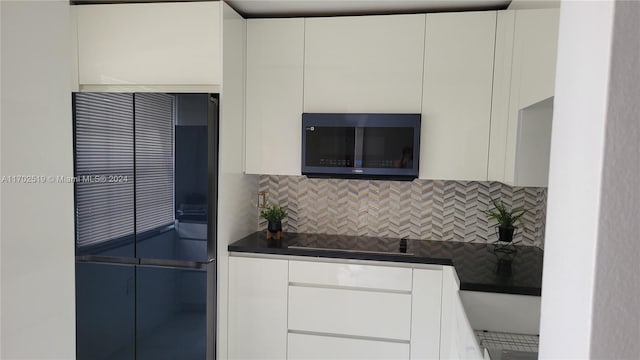 kitchen featuring tasteful backsplash, white cabinetry, black electric stovetop, and fridge