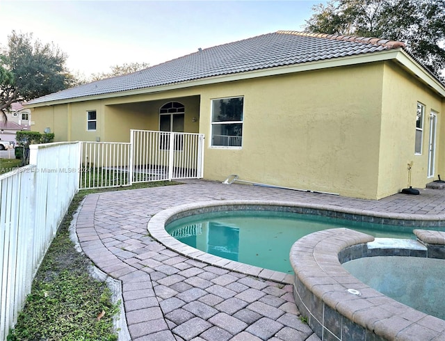 rear view of house with a swimming pool with hot tub and a patio