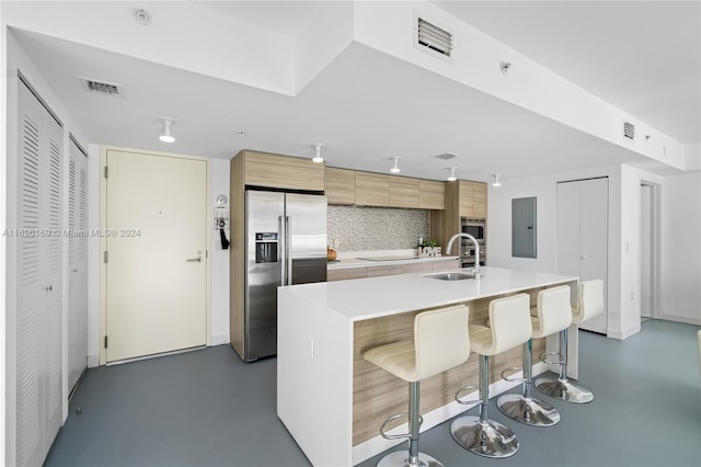 kitchen with a kitchen bar, stainless steel fridge, decorative backsplash, sink, and a center island with sink