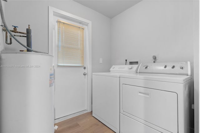 clothes washing area with washing machine and dryer, light wood-type flooring, and water heater