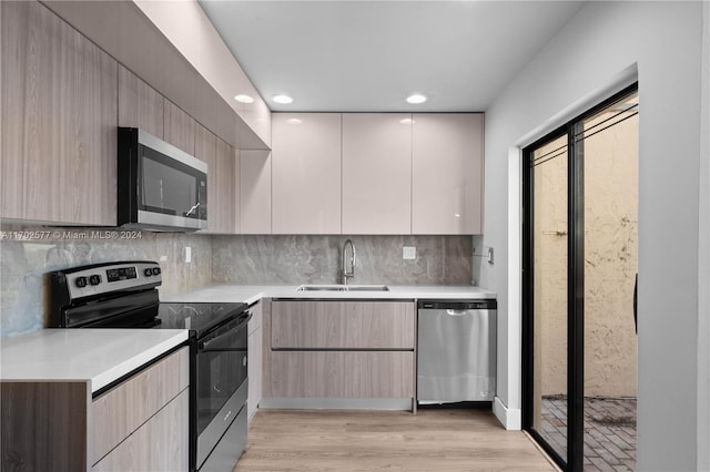 kitchen featuring appliances with stainless steel finishes, backsplash, light hardwood / wood-style flooring, and sink