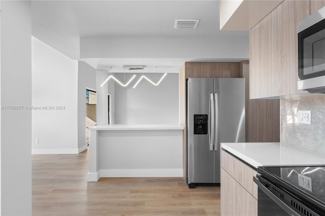 kitchen with backsplash, light hardwood / wood-style floors, and appliances with stainless steel finishes