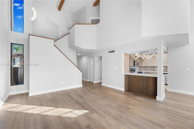 unfurnished living room with beamed ceiling, high vaulted ceiling, and light hardwood / wood-style flooring