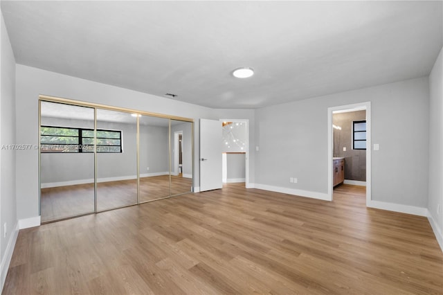 unfurnished bedroom featuring light wood-type flooring, ensuite bath, and a closet