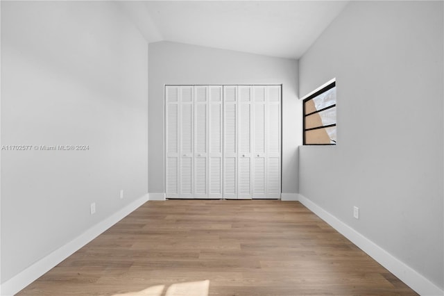 unfurnished bedroom with light hardwood / wood-style floors, lofted ceiling, and a closet