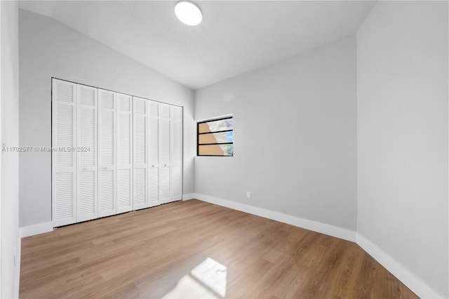 unfurnished bedroom featuring lofted ceiling, light wood-type flooring, and a closet