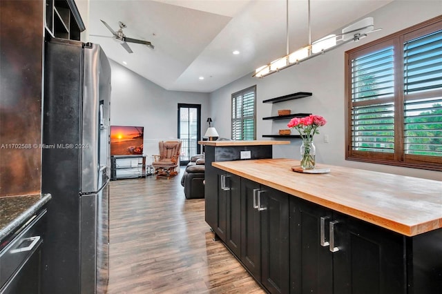 kitchen featuring hanging light fixtures, vaulted ceiling, hardwood / wood-style flooring, stainless steel fridge, and butcher block counters