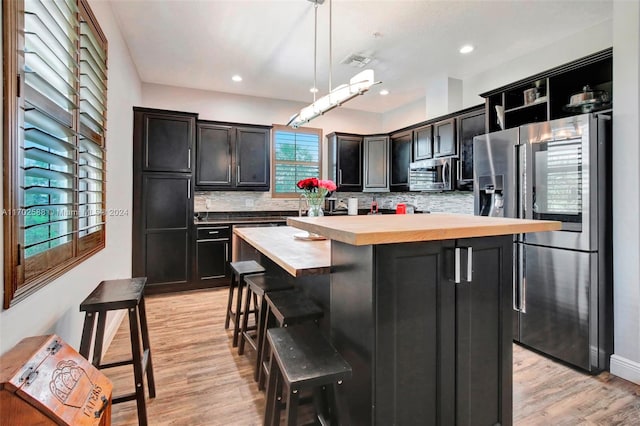 kitchen featuring wood counters, a center island, decorative light fixtures, a healthy amount of sunlight, and stainless steel appliances