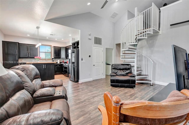 living room featuring ceiling fan, high vaulted ceiling, and light hardwood / wood-style flooring