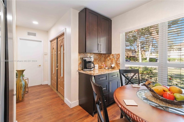 kitchen with a wealth of natural light, dark brown cabinets, light stone countertops, and light hardwood / wood-style flooring