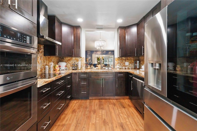 kitchen featuring sink, wall chimney exhaust hood, hanging light fixtures, appliances with stainless steel finishes, and light wood-type flooring