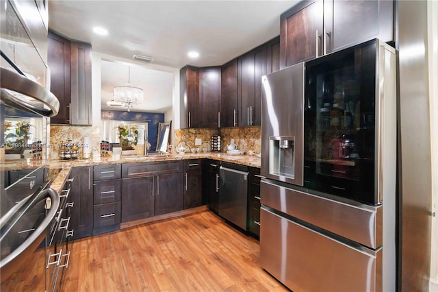 kitchen featuring appliances with stainless steel finishes, tasteful backsplash, pendant lighting, a chandelier, and light hardwood / wood-style floors