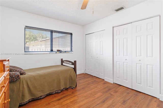 bedroom featuring hardwood / wood-style floors, ceiling fan, a textured ceiling, and two closets